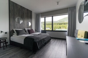A modern hotel room with a large bed, a desk, and a view of a green landscape through the window. - Fosshotel Husavik (Husavik)