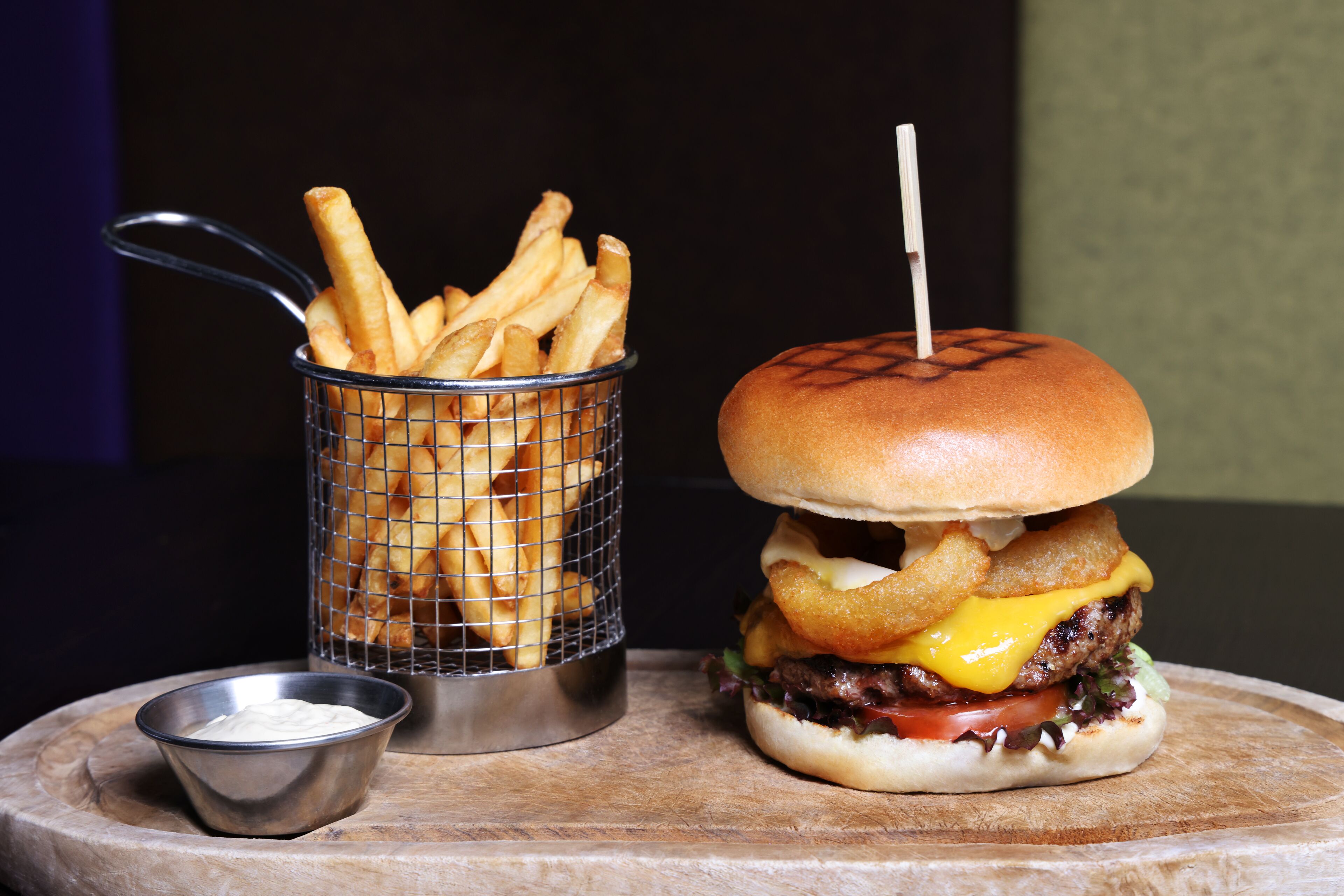 A burger with a bun, cheese, lettuce, tomato, and a side of fries in a basket.