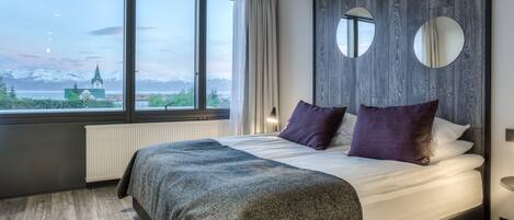Ein modernes Hotelzimmer mit einem großen Bett, Blick auf Berge und einer Holzvertäfelung.
