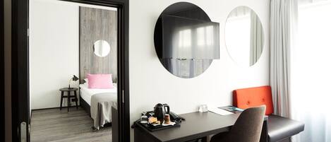 A hotel room with a bed, a desk, a chair, a coffee maker, and a mirror.