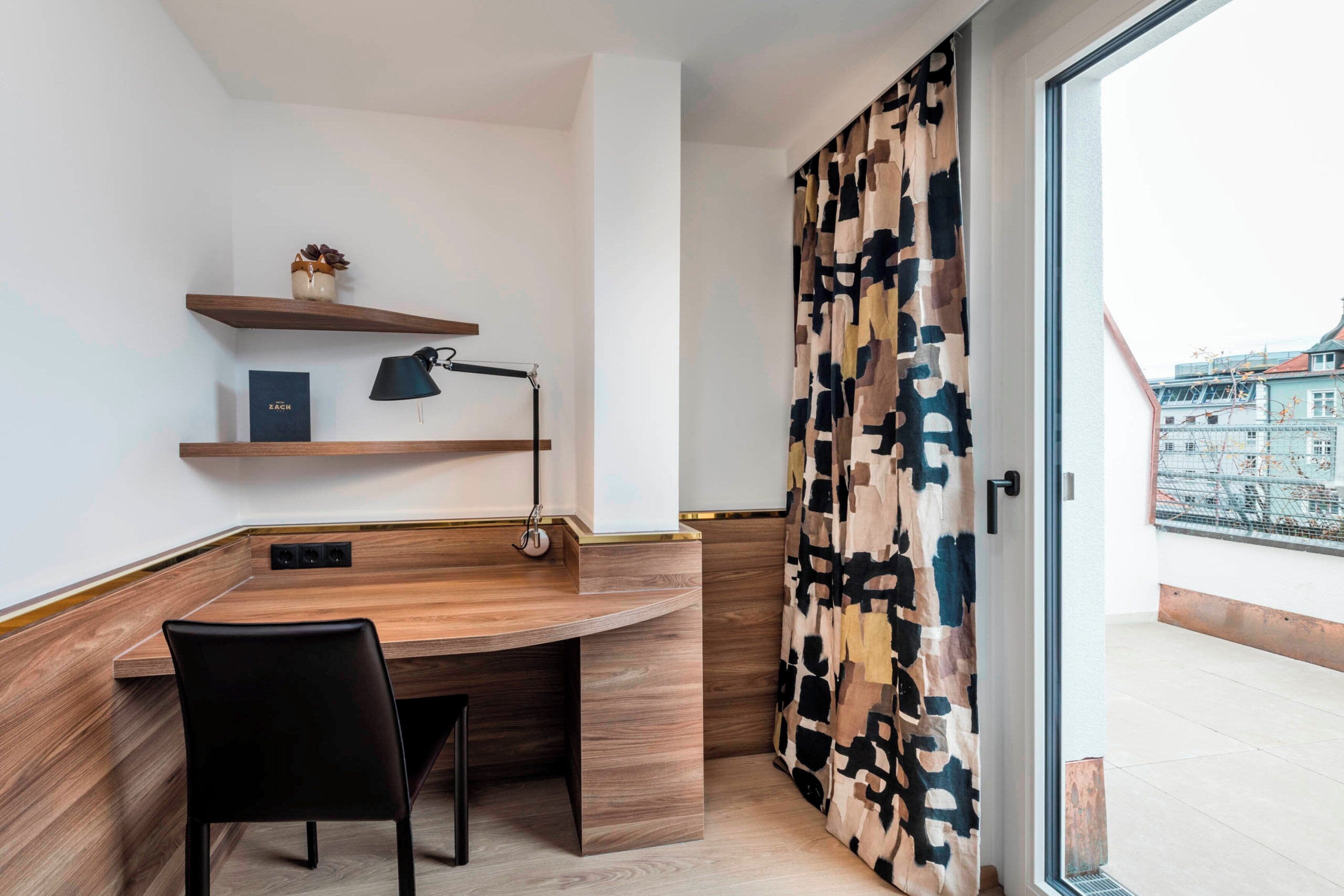Een moderne kamer met een houten bureau, een zwarte stoel, een lamp en een kamerkleed.