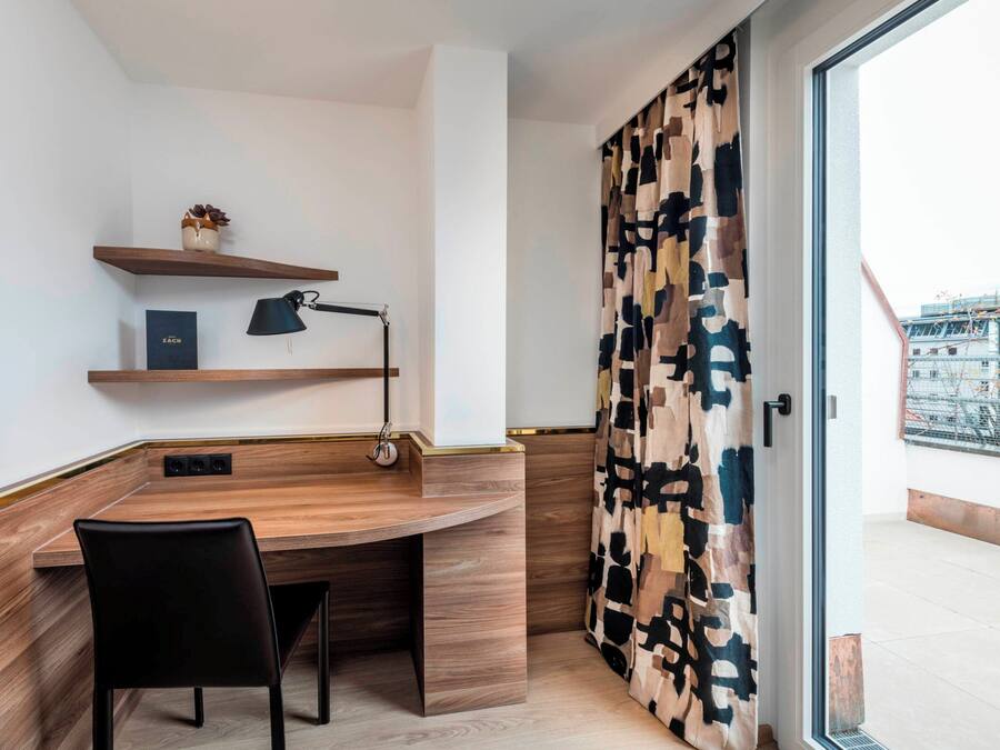 Een moderne kamer met een houten bureau, een zwarte stoel, een lamp en een kamerkleed.