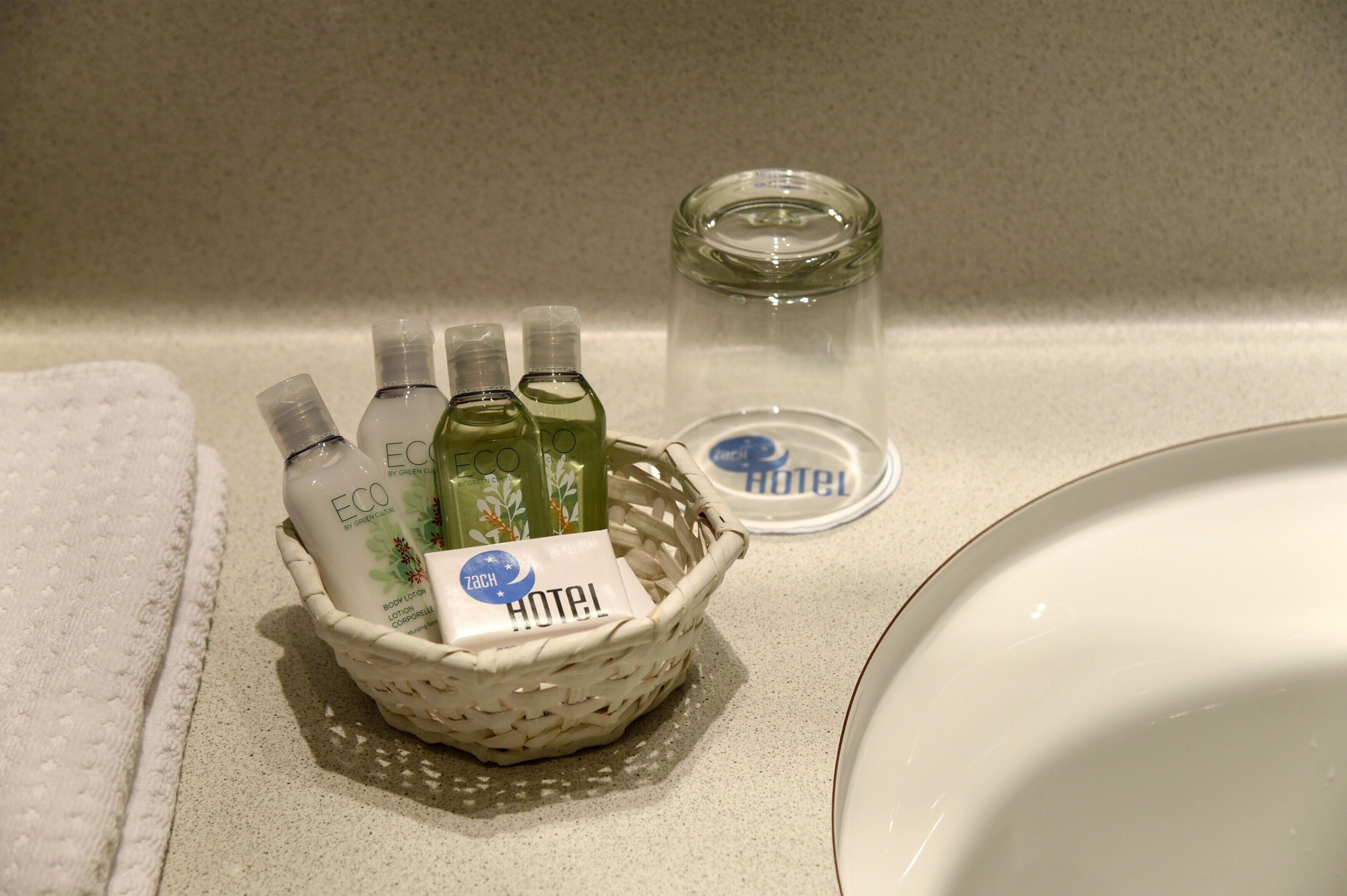 A bathroom counter with a white towel, a small basket containing toiletries, and a glass of water.
