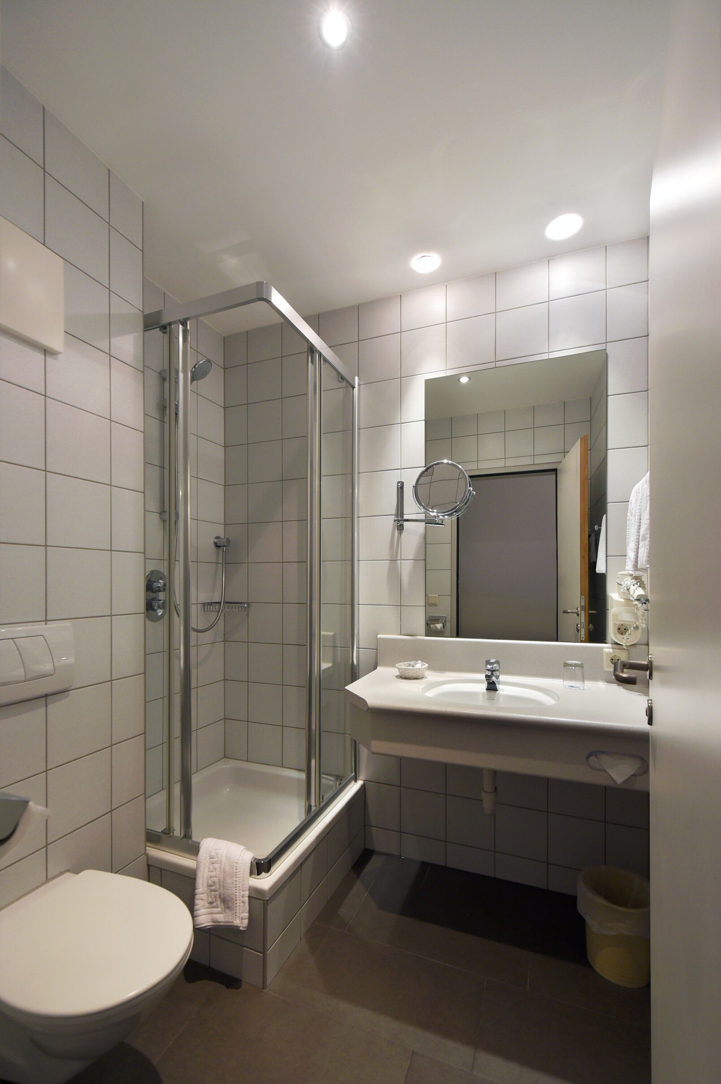 A modern bathroom with a glass-enclosed shower, a white sink, and a large mirror.