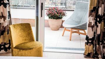 A room with a golden chair, a wicker chair, and a potted plant outside a sliding glass door.