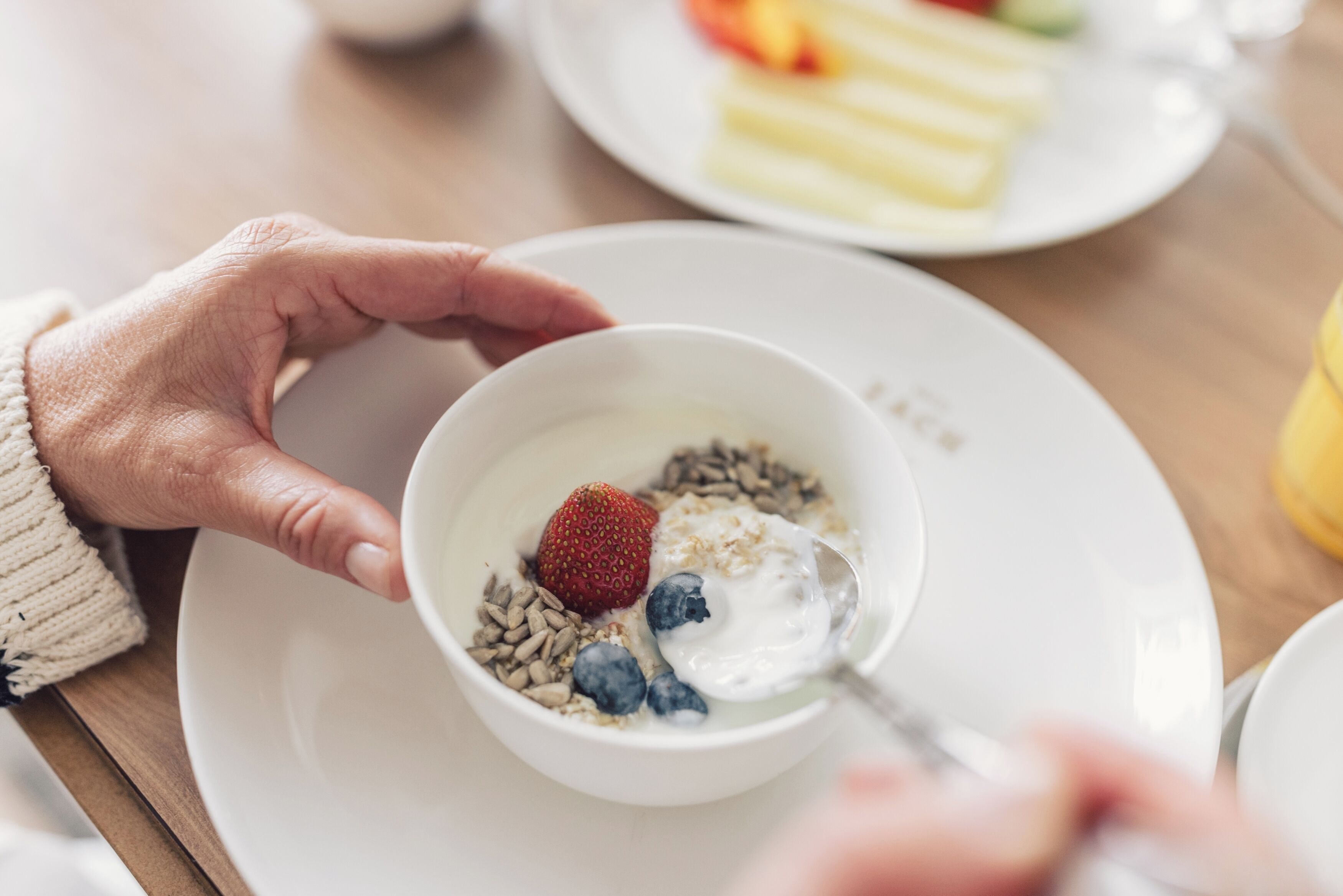 A bowl of cereal with strawberries and blueberries on a white plate.