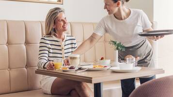 Ein modernes Wohnzimmer mit einer Couch, einem Esstisch mit Frühstücksgebäck und einer Person, die Essen serviert.