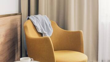 A hotel room with a mustard-colored armchair, a small white side table with a cup, and a brown bag on the floor.