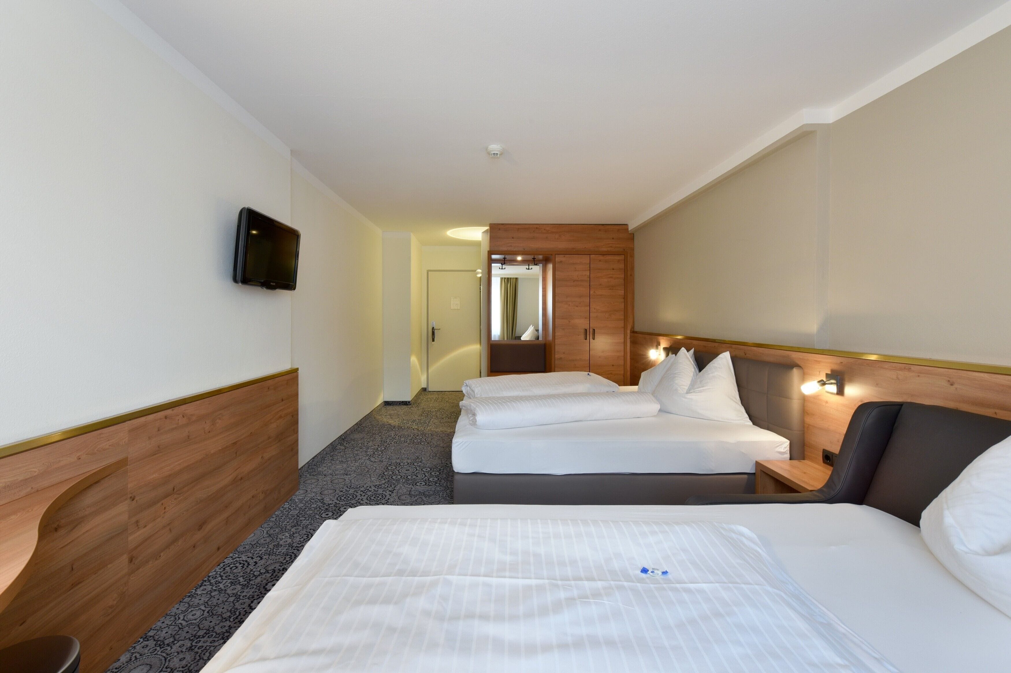 A hotel room with a large bed, a smaller bed, a desk, and a TV mounted on the wall.