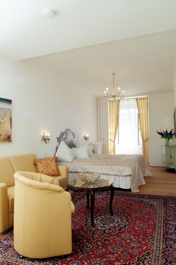 A bedroom with a bed, a sofa, a chandelier, and a large rug.
