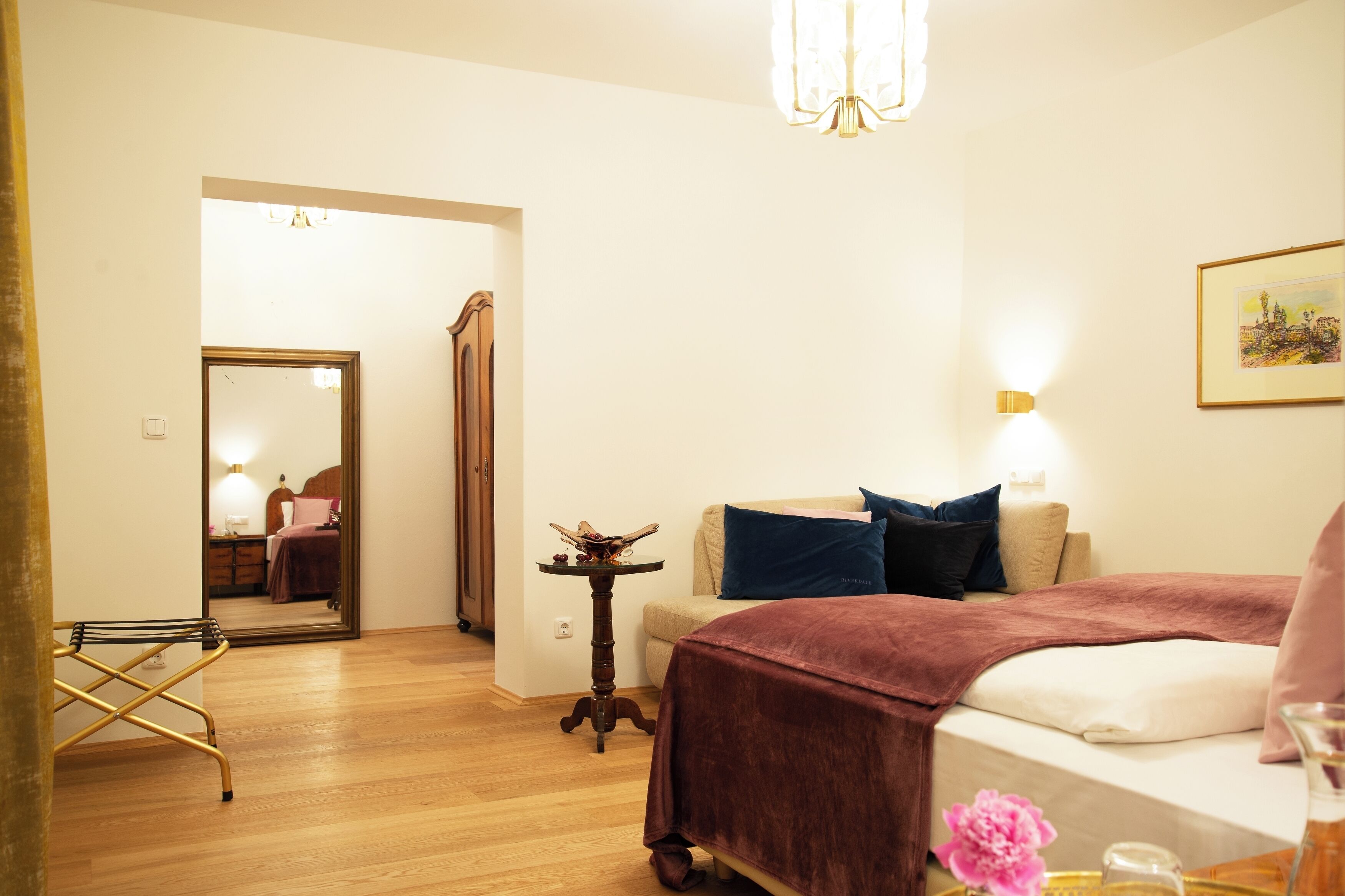 A hotel room with a bed, a small table, a mirror, and a door leading to another room.