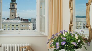 A room with a view of a tower, a chair, a dresser with a mirror, and a window with curtains.
