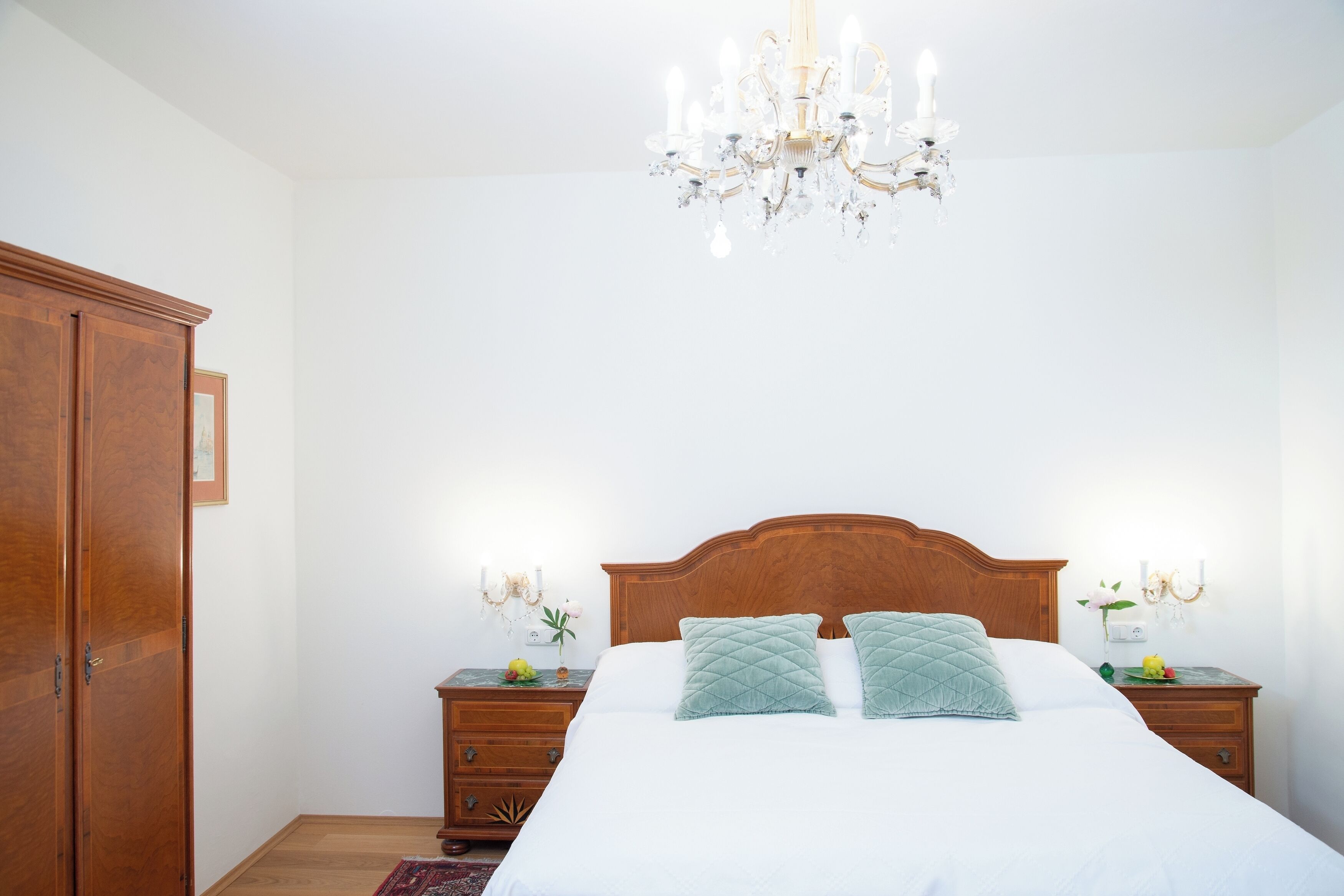 A bedroom with a wooden bed, two nightstands, a chandelier, and a wardrobe.