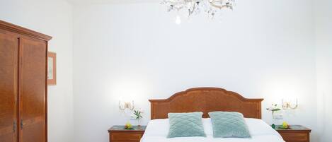 A bedroom with a wooden bed, two nightstands, a chandelier, and a wardrobe.