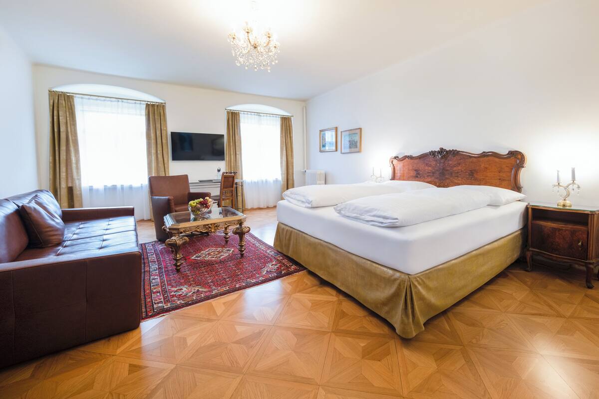 A hotel room with a large bed, a sofa, a TV, and a chandelier.
