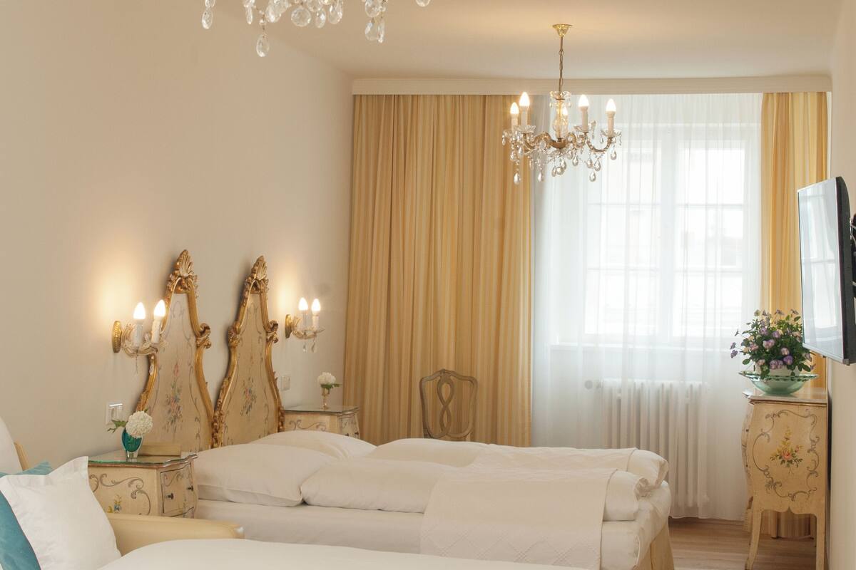 A hotel room with two beds, a chandelier, a television, and a window with curtains.