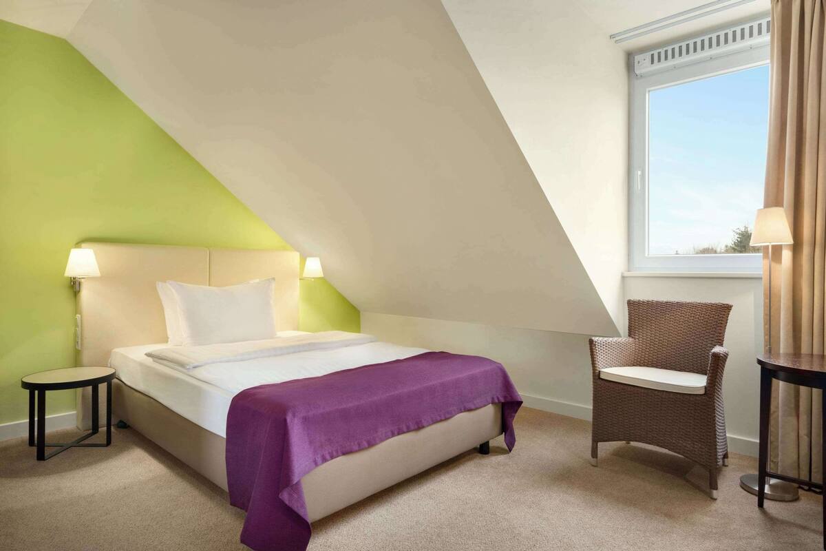 A bedroom with a bed, a chair, a table, and a window.