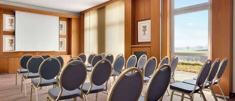 Un salón de conferencias con filas de sillas, una pizarra y cuadros en las paredes.