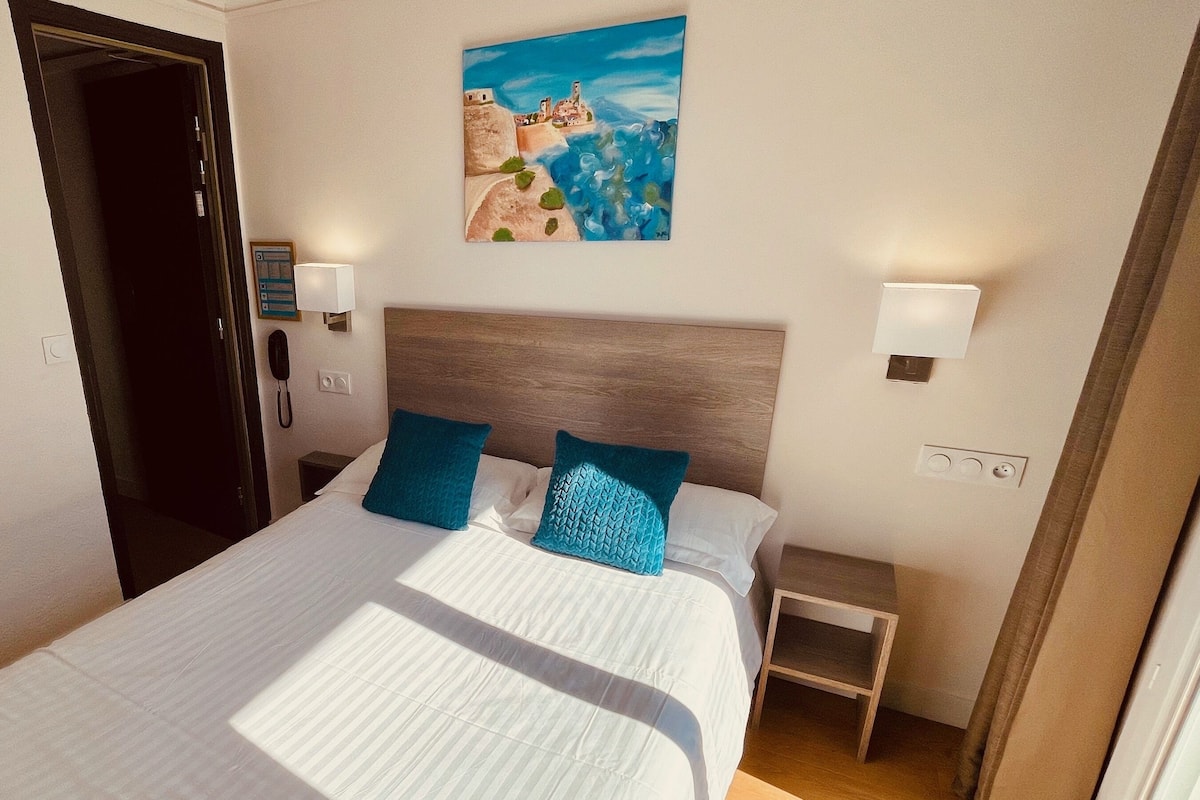 Una habitación de hotel con cama, un cuadro en la pared, un teléfono y una mesita de noche.