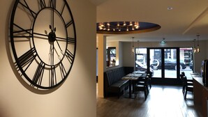 A modern interior with a large wall clock, seating area, and a view of the street outside. - Hôtel Courbet (Antibes)