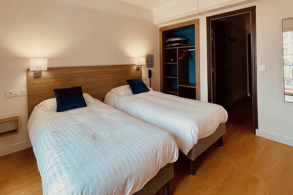 Habitación de hotel con dos camas individuales, cabecera de madera, armario y espejo.