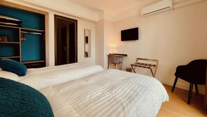 A hotel room with a large bed, a desk with a chair, a TV mounted on the wall, and a wardrobe with a mirror. - Hôtel Courbet (Antibes)