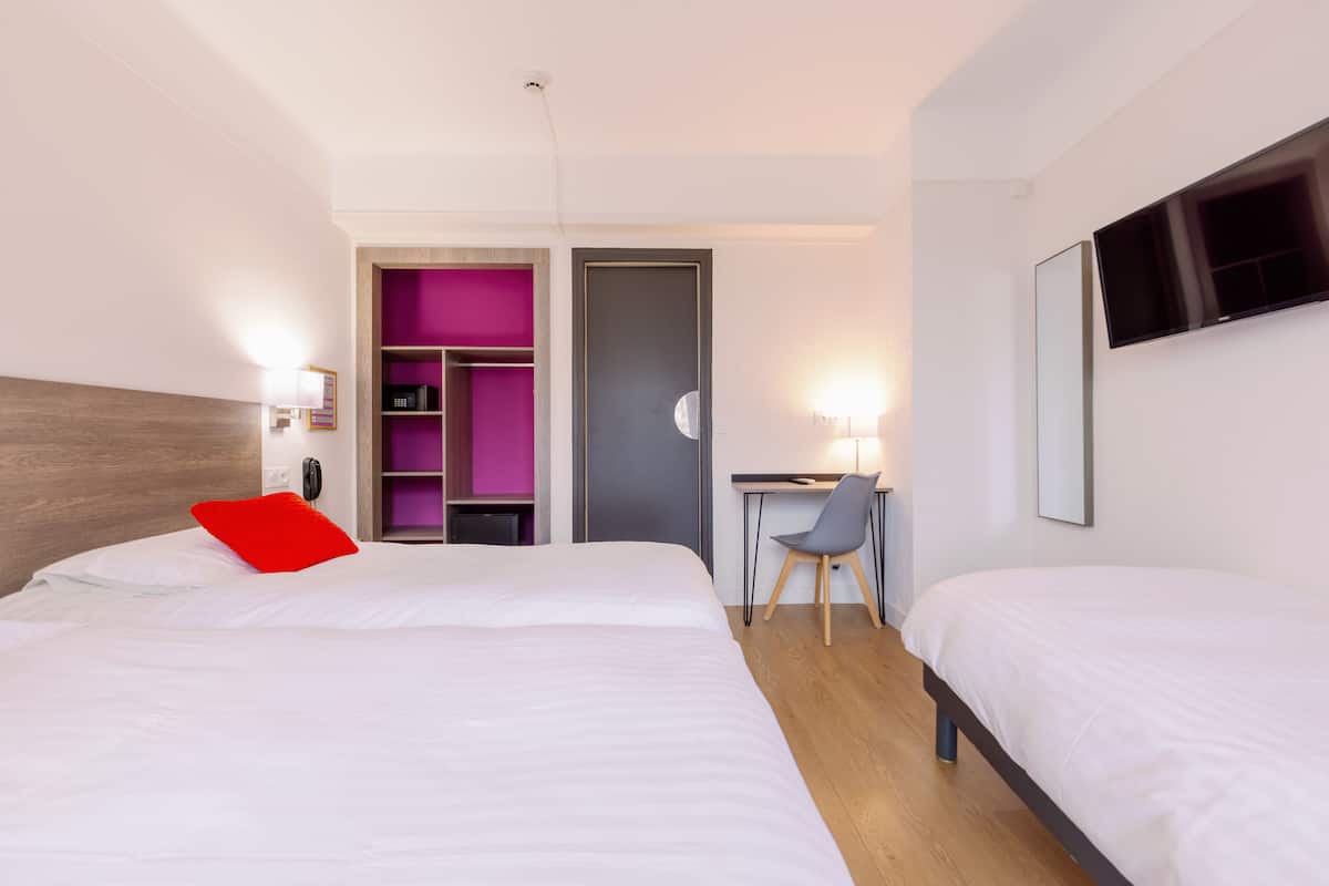 Habitación de hotel con una cama grande, un escritorio y una silla. Se ve un armario con interior morado y un televisor montado en la pared.