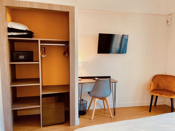 Une chambre d’hôtel avec une armoire en bois, un bureau avec une chaise, un téléviseur fixé au mur et un lit.