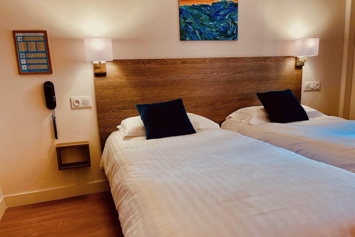 Habitación de hotel con dos camas, cabecera de madera, un cuadro, un teléfono y una mesita.