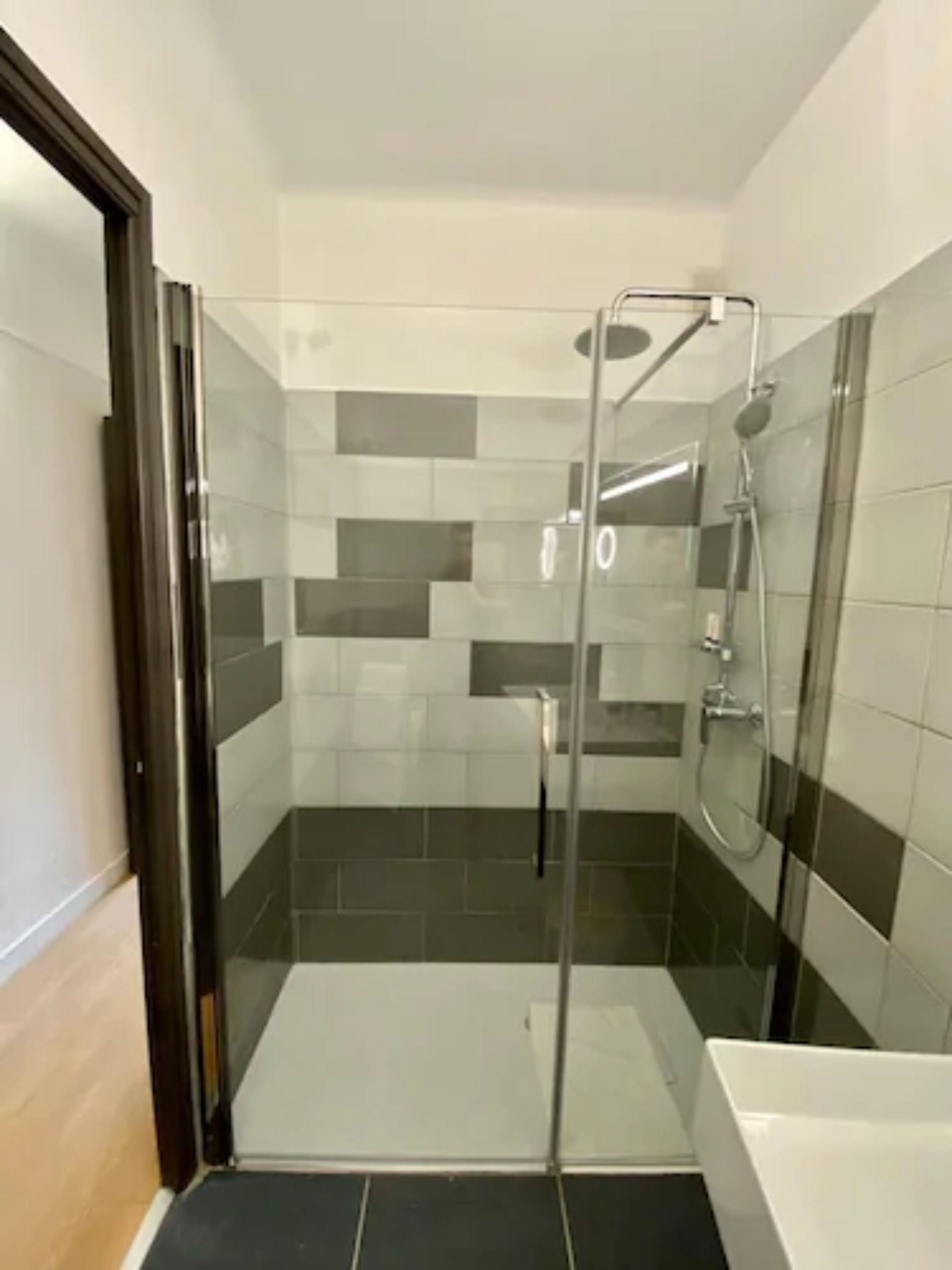 Une salle de bain moderne dotée d’une douche à parois de verre, de murs carrelés et d’un espace séparé pour la baignoire.