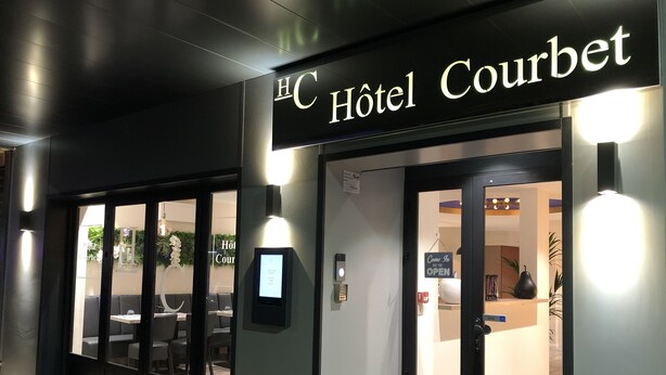 The exterior of HC Hotel Courbet with a modern facade, a digital display, and a 'Come In We're Open' sign. - Hôtel Courbet (Antibes)