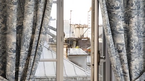A view through a window with curtains depicting historical scenes, overlooking a building with a flat roof and visible structural elements. - Odéon Hôtel  (Paris)