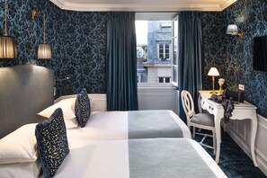 Une chambre d’hôtel avec deux lits, un bureau, une chaise, une lampe et une vue sur la ville par la fenêtre.