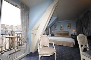 A hotel room with a bed, two chairs, a small table, and a balcony with a view of the city.