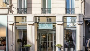 A hotel facade with a sign reading "HOTEL," large windows, and a potted plant in front. - Hôtel Ducs D'Anjou (Paris)