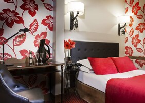 A hotel room with a bed, a desk, a chair, a lamp, and a telephone.