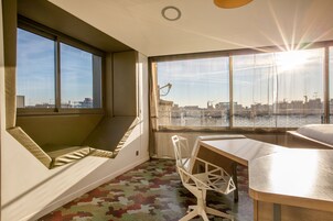A modern room with a large window, a desk, and a cushioned seating area.