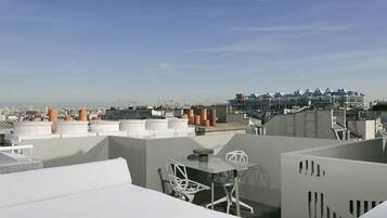 Terraza en la azotea con una mesa y sillas, rodeada de edificios modernos y un cielo despejado.