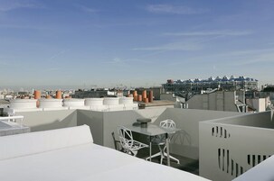 Terraza en la azotea con una mesa y sillas, rodeada de edificios modernos y un cielo despejado.