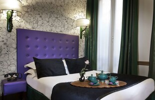 A bedroom with a purple headboard, a bed with black and white bedding, a bedside table with a telephone, and a tray with teacups and a teapot.