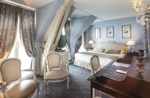 Una habitación de hotel con una cama, dos sillones, un escritorio y un piano.