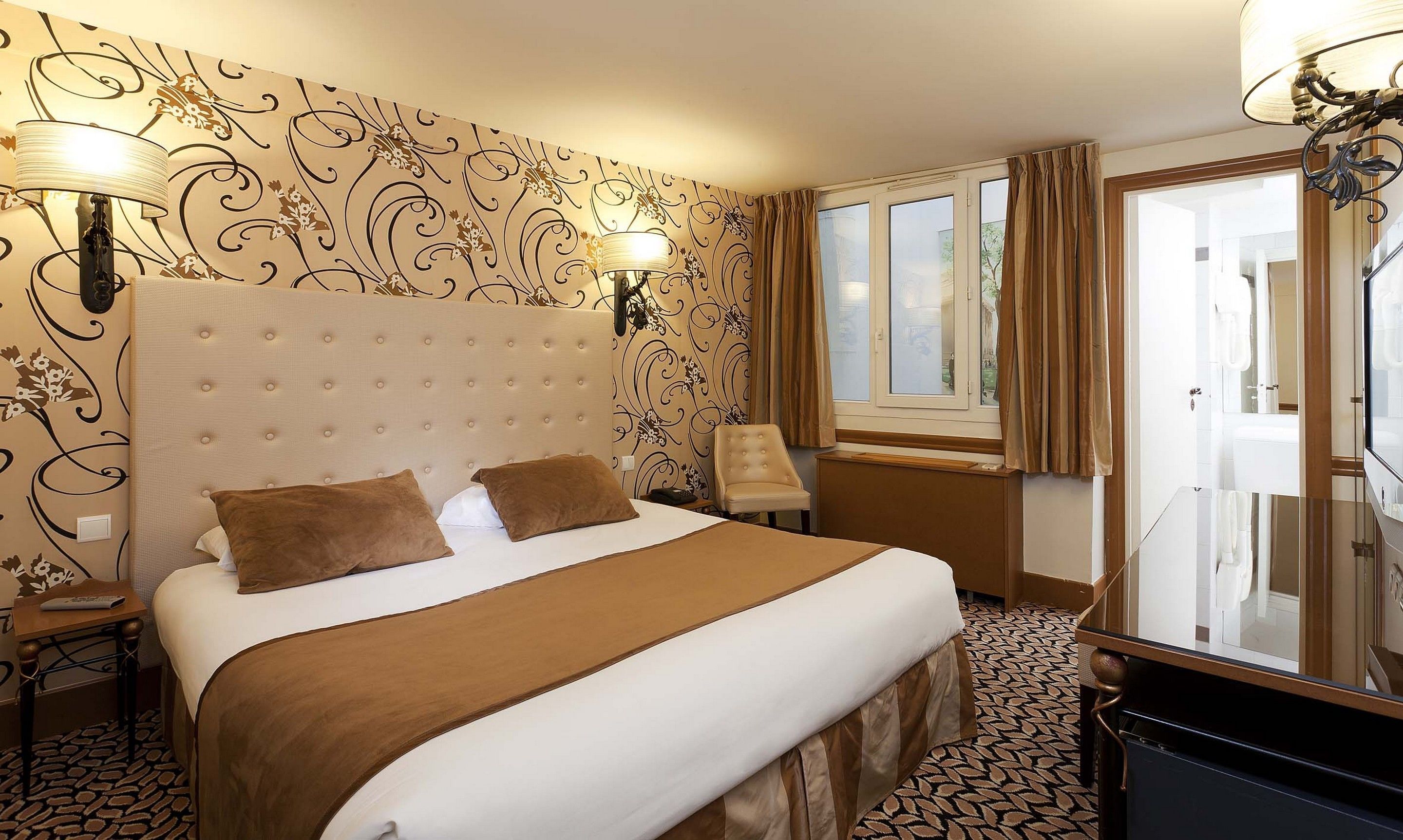 A hotel room with a large bed, two bedside lamps, a chair, a desk, and a window with curtains.