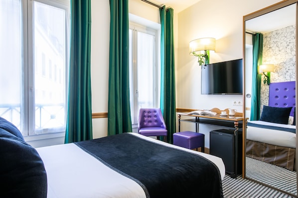 Una habitación de hotel con cama, escritorio, silla, televisor y espejo.
