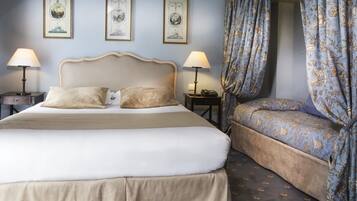 A hotel room with a large bed, a smaller sofa, two bedside tables with lamps, and a curtain with a floral pattern.