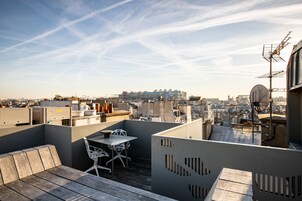 Una terrazza sul tetto con un tavolo e sedie, una panca di legno e vista sulla città.