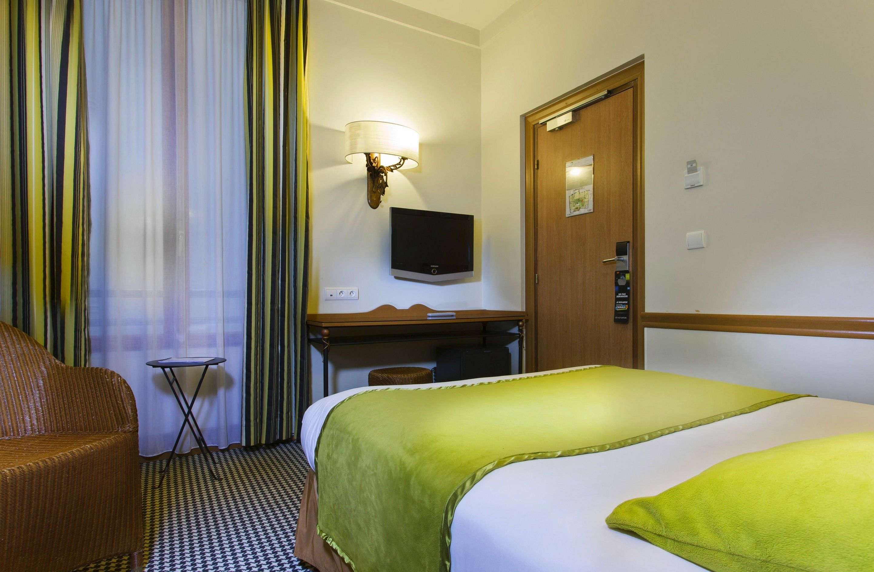 A hotel room with a bed, a desk, a television, and a door.