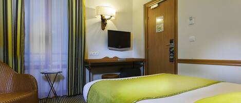 A hotel room with a bed, a desk, a television, and a door.
