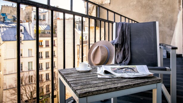 A balcony with a wooden table, a white cup, a hat, and a newspaper. - Hôtel Ducs D'Anjou (Paris)