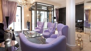 A modern living room with purple armchairs, a glass coffee table, and a decorative Buddha statue. - Hôtel Ducs D'Anjou (Paris)