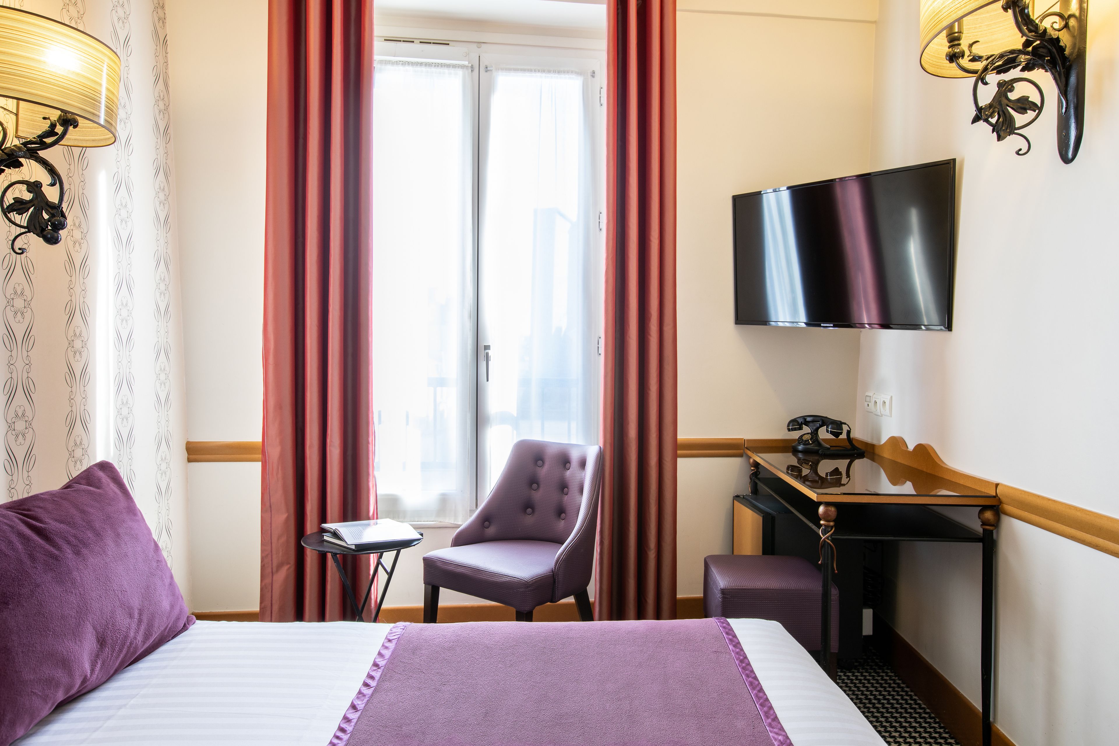 A hotel room with a bed, a chair, a desk, and a TV.
